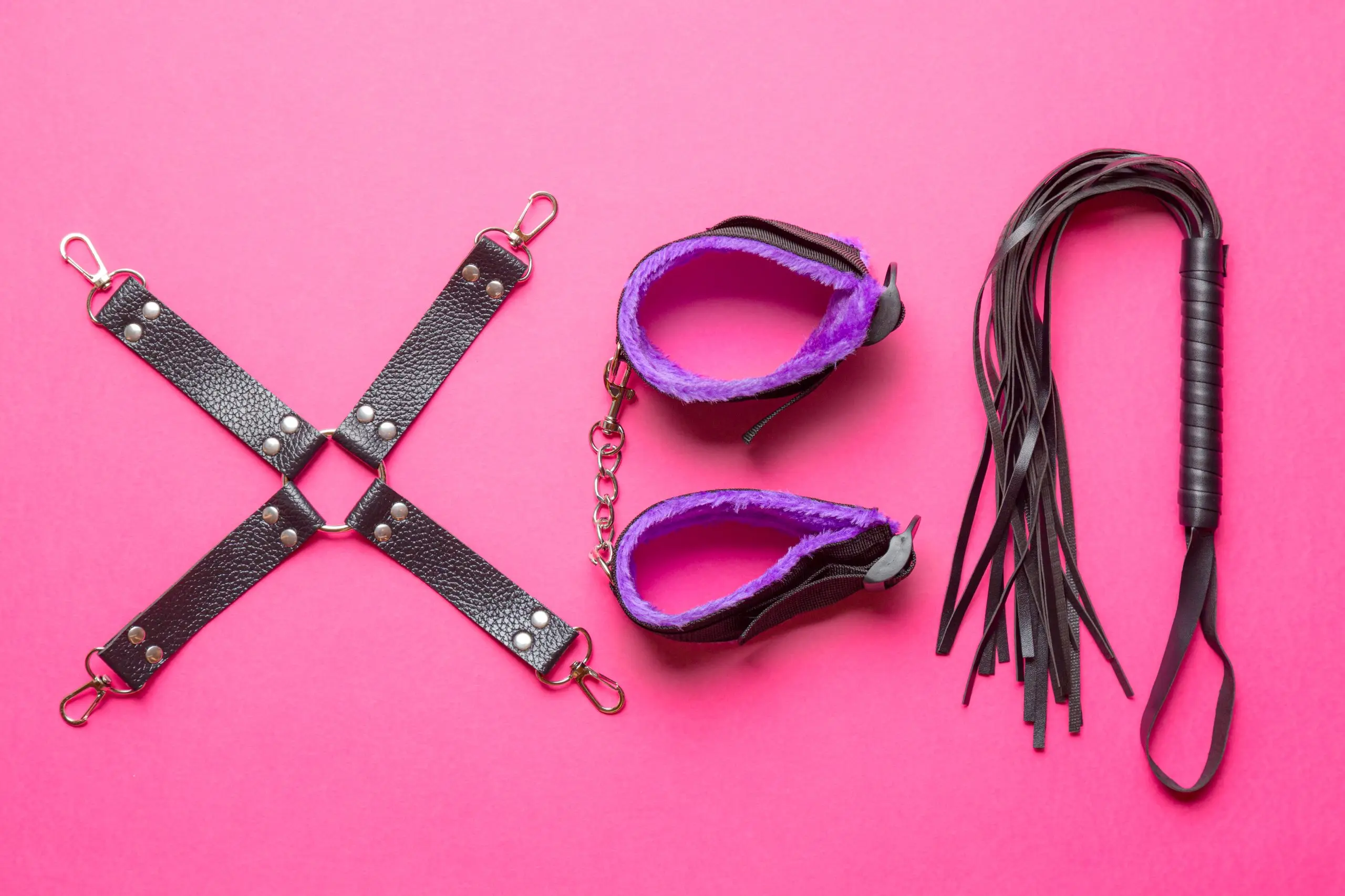Akcesoria BDSM – kajdanki, pejcz i knebel na czerwonym tle
